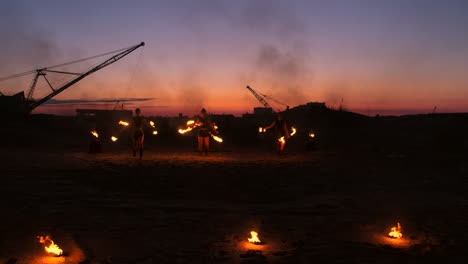 Fire-show-three-women-in-their-hands-twist-burning-spears-and-fans-in-the-sand-with-a-man-with-two-flamethrowers-in-slow-motion